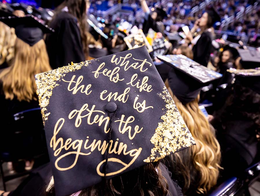 Black mortar board graduation cap that reads in gold lettering, "What feels like the end is often the beginning"