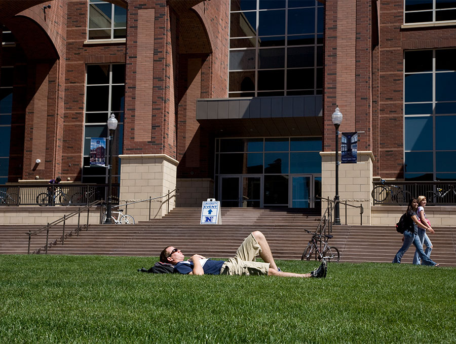 A student laying on a grass in front of a library building