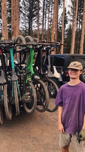 A man standing in front of parked cars and bicycles. 