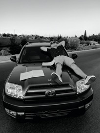 A modern black and white image of a man with sunglasses and laying on top of his black truck.