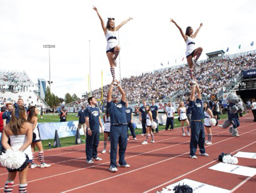 Two University of Nevada, Reno cheerleaders are balanced in the air as a roaring football crowd looks on. 