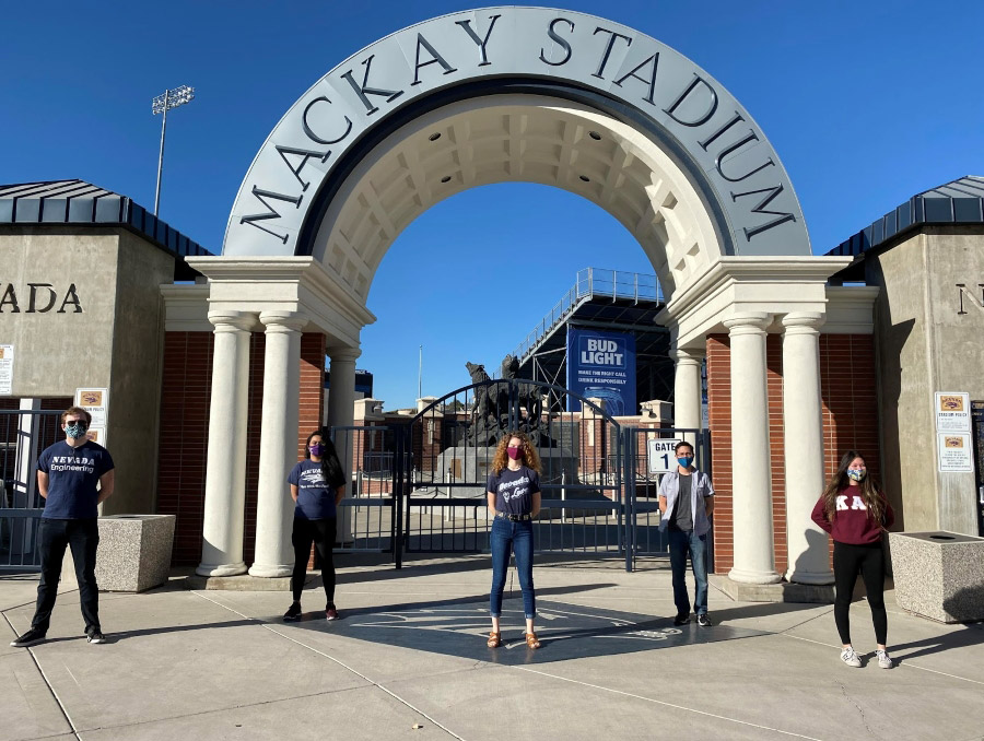 Students are standing under the Mackay Stadium entrance arch, mimicking a similar photo that was taken a century ago
