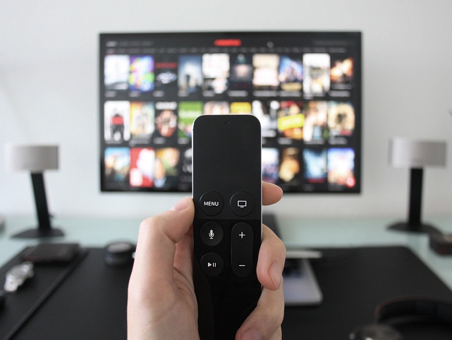 Person pointing a TV remote at a television screen with different TV programs.