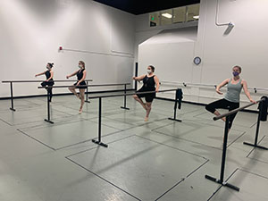 ballet dancers masked stand at the barre