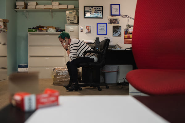 Melissa Taylor sits in a chair holding a cell phone to her ear at her desk at the Little Reno Theater.