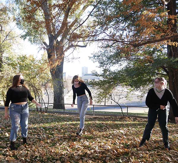 Three team members play outside in the leaves on campus