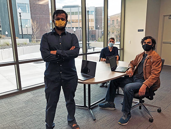 Three people gathered around a table, all wearing masks