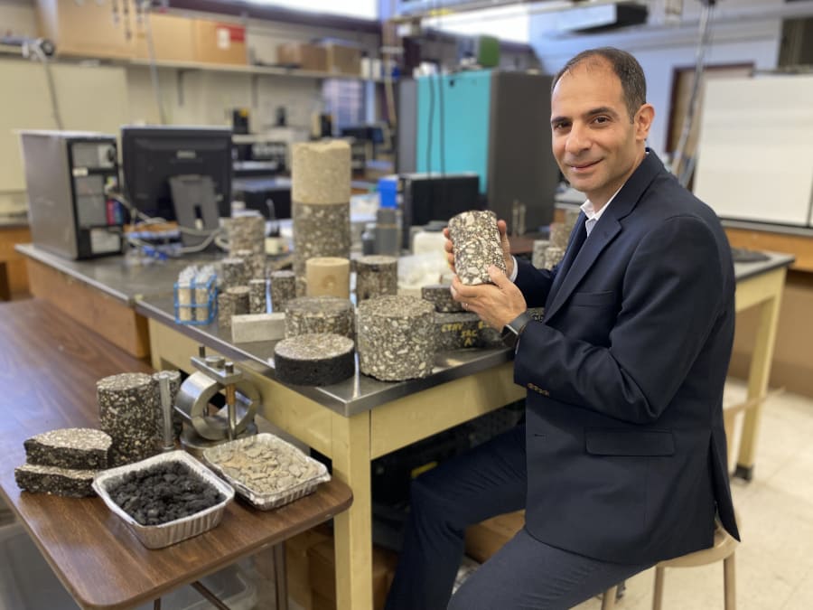 University Civil and Environment Engineering Professor Elie Y. Hajj sits at a workable in a pavement lab, holding an asphalt sample.