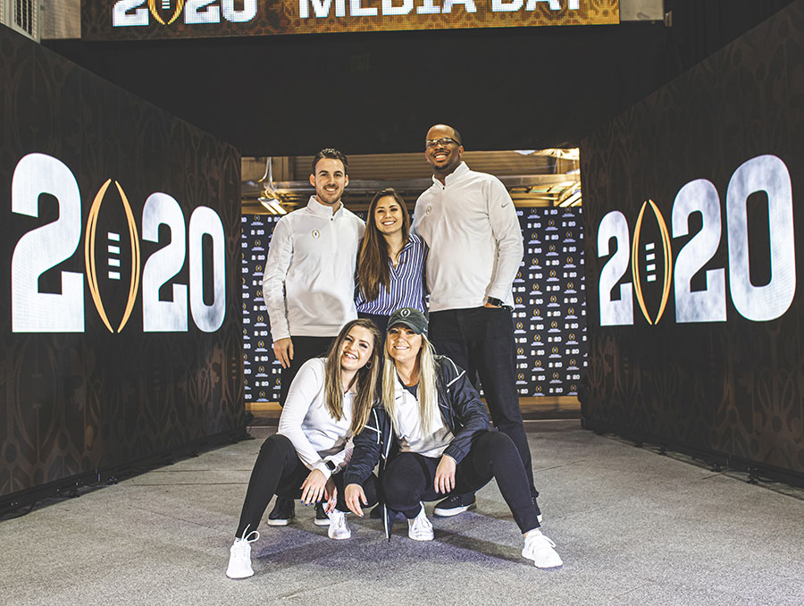 Five university alumni pose in front of a stadium tunnel at the College Football Playoff.