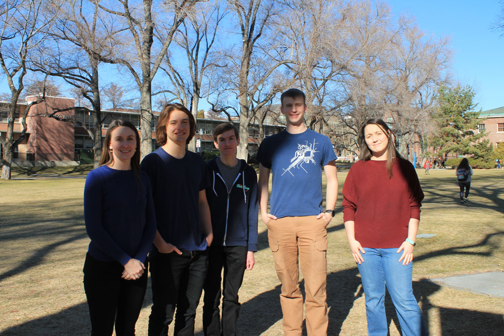 A group of students and their professor are standing on the Quad.