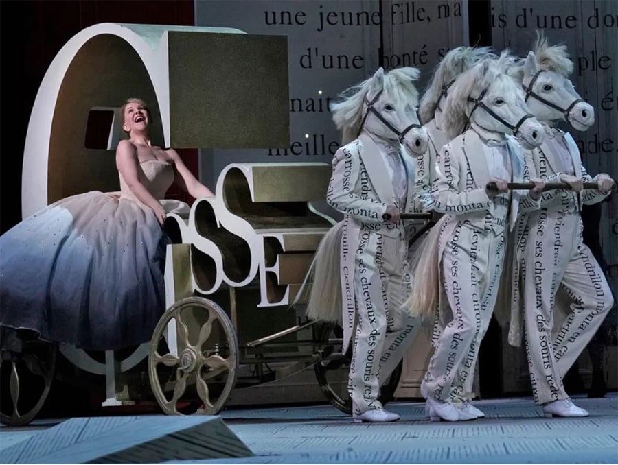 An image from the opera Cendrillon by Massenet. Cinderella is being pulled by men in white suits wearing horse masks. 