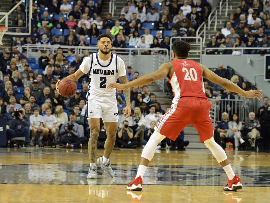 Nevada basketball guard Jalen Harris, wearing white with blue 2 on his jersey, dribbles against a UNLV opponent in red.