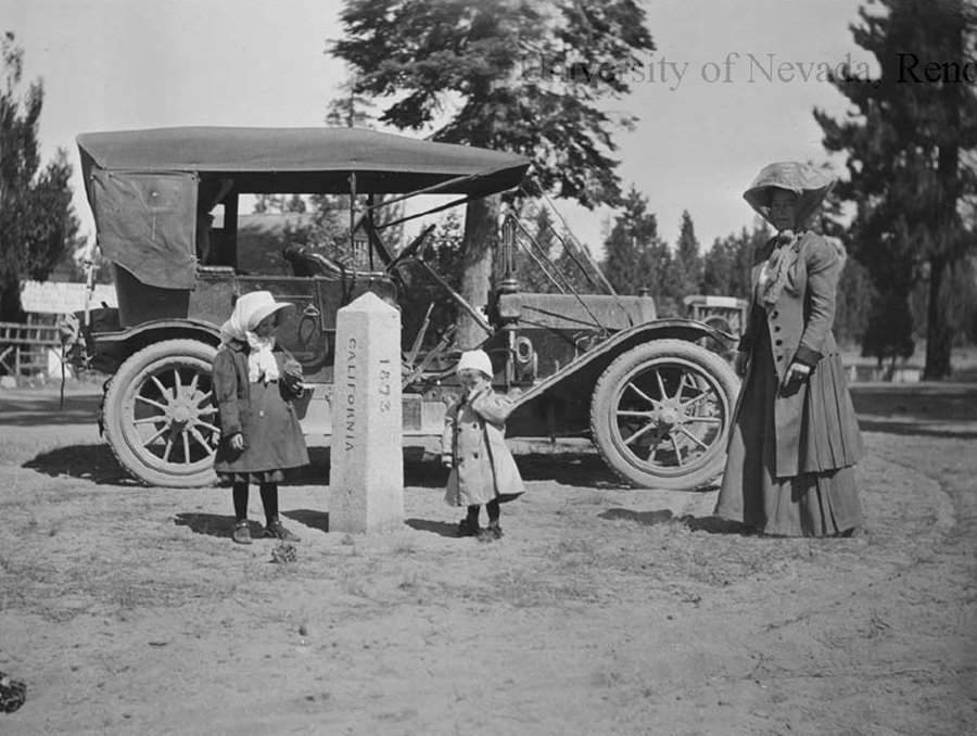 A black and white image of a woman and children next to a car