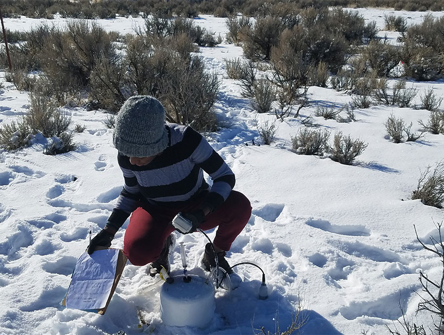 Christina kneeling on a range in the snow with lab equipment