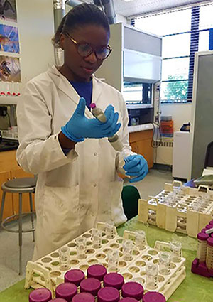 Christina wearing a lab coat and gloves testing samples in a lab.