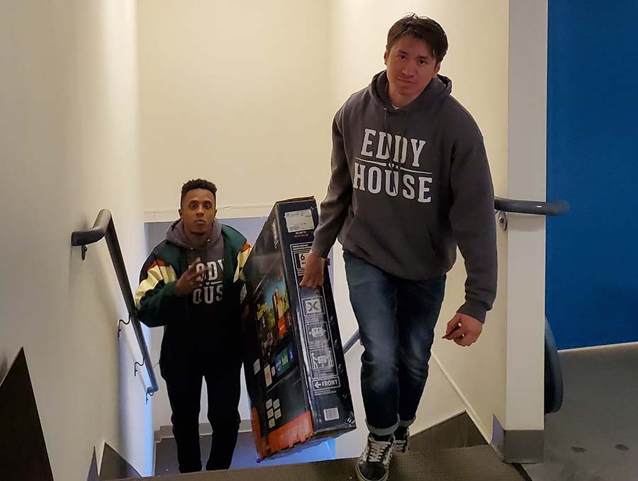 Two Eddy House Youth Advocates carry a TV box up stairs 
