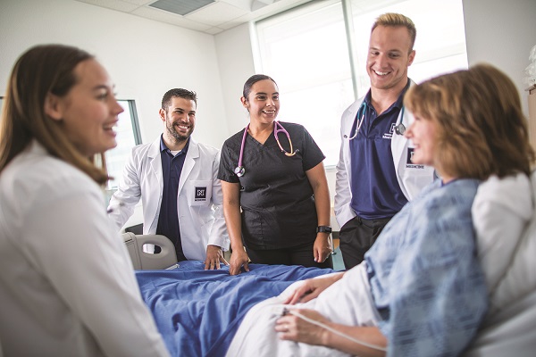 A women in a hospital bed with University doctors and nurses around her