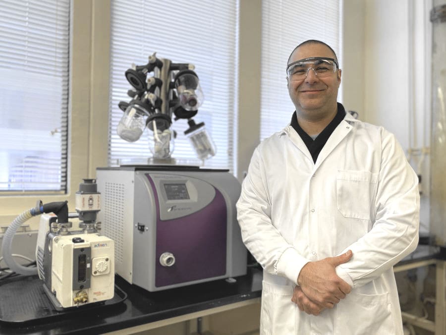 Researcher Yftah Tal-Gan in a white lab coat and safety glasses standing near lab equipment