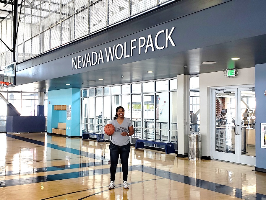 Sheena Harvey holds a basketball while standing under the words Nevada Wolf Pack in the E.L. Wiegand Fitness Center