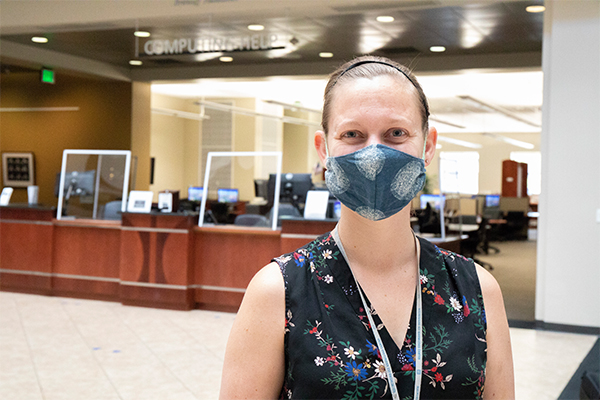 Woman wearing a facial covering standing in front of the Access Serviced Desk located on the second floor of the Mathewson-IGT Knowledge Center 