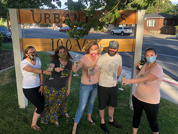 People stand outdoors holding champagne glasses in front of a sign that read Urban Roots.