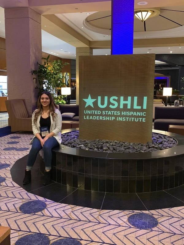 Gabriela Meza sitting next to the USHLI entryway sign