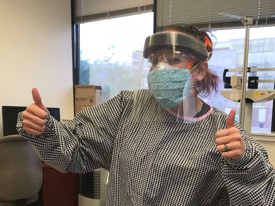 A healthcare worker wearing a gown, face mask, and face shield giving the thumbs up