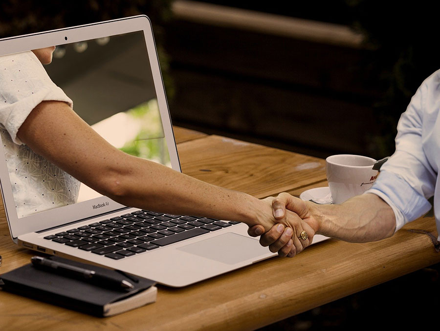 Two people shaking hands with one hand extending from a computer screen