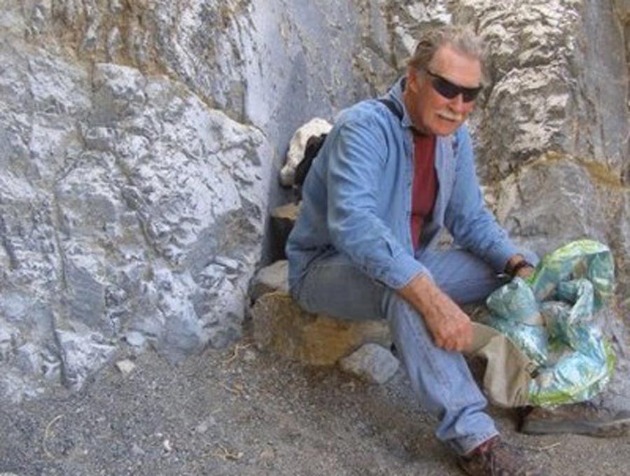 Photo of Tommy Thompson sitting at the base of a rock face holding a map.