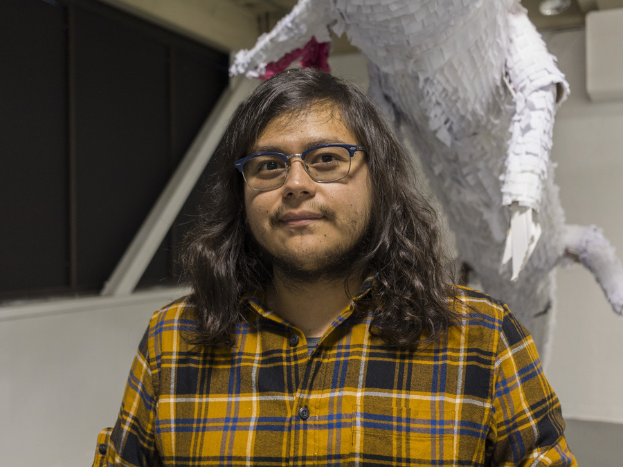 Undergraduate Research awardee Cesar Piedra stands in front of his sculptural project: a white animal figure with a textured paper surface.