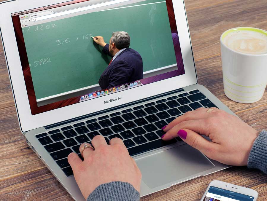 laptop screen showing man writing on green chalkbpard