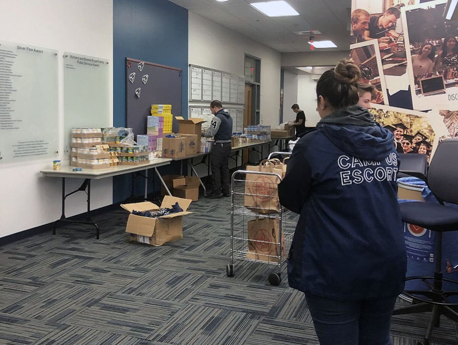 A grocery assembly line with social-distanced volunteers working and a Campus Escort worker in the foreground