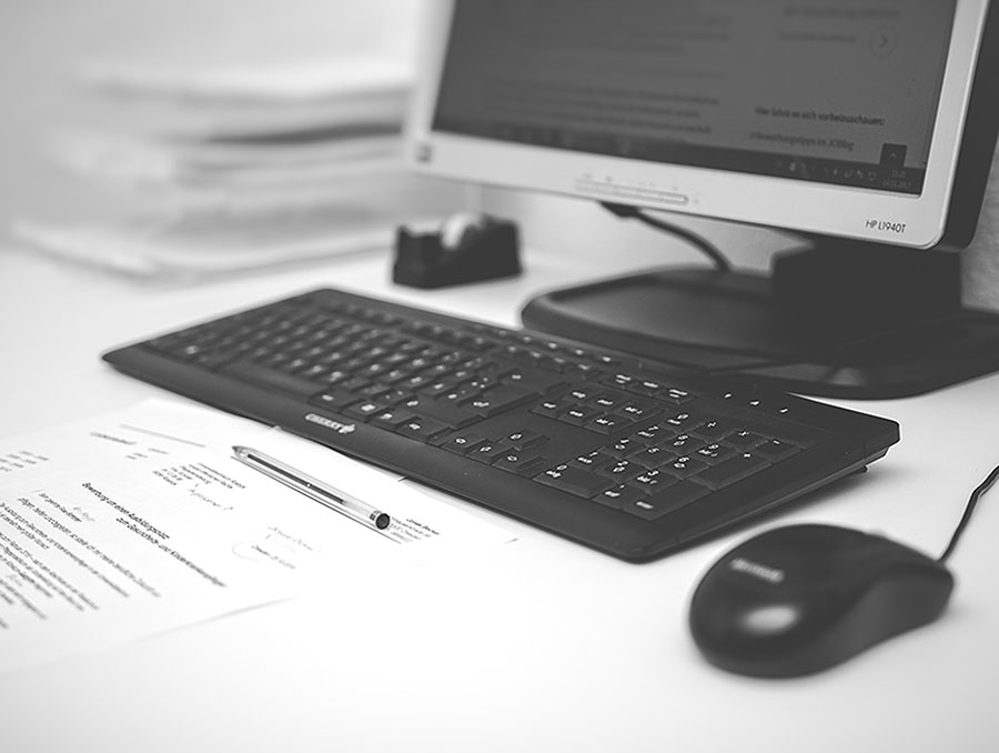 Desk with a computer, mouse, paper and pen.