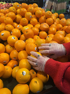 Shopping Angels volunteer picks out oranges with gloved hands while grocery shopping