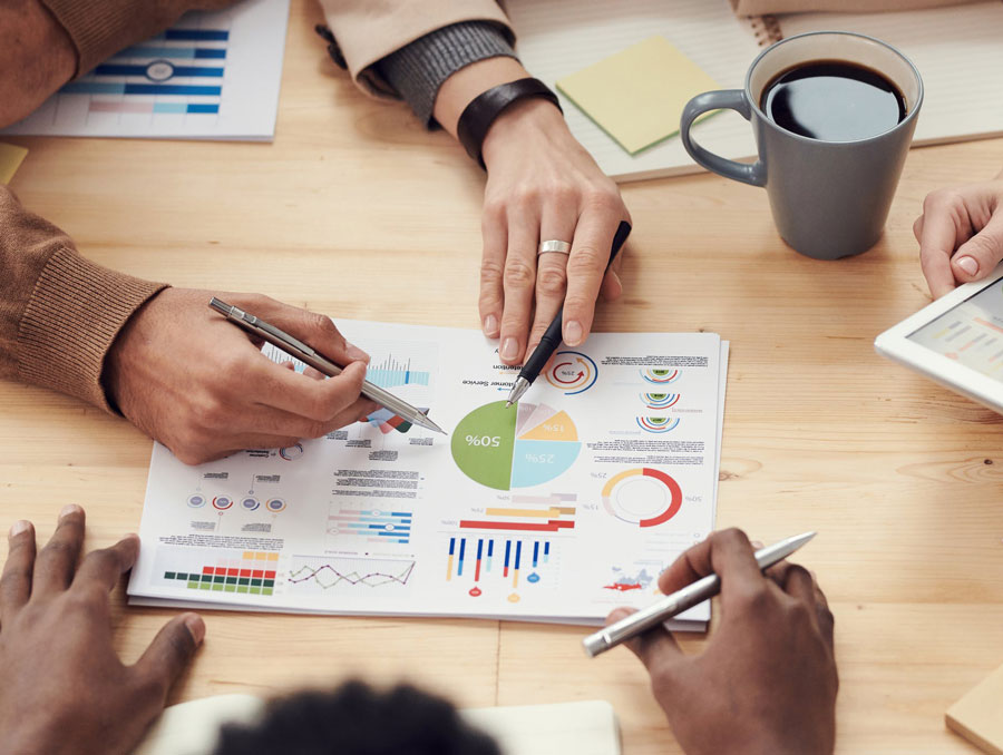 People around a desk analyzing business related charts and graphs both printed and on a tablet.