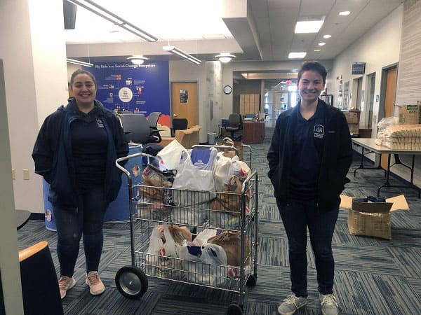 Students smiling next to a cart loaded with groceries and supplies