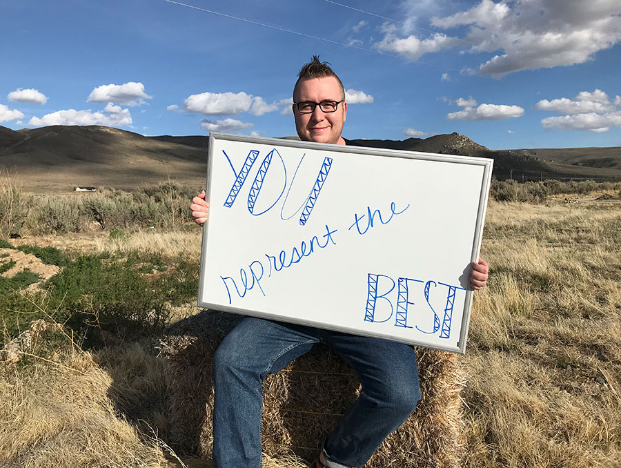 Ian Hartshorn sitting outside holding a sign that reads "you represent the best."