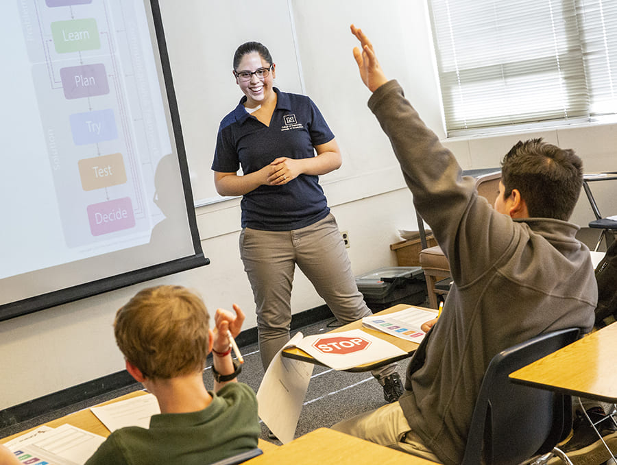 Student raising hand while Ambassador stands at front of class