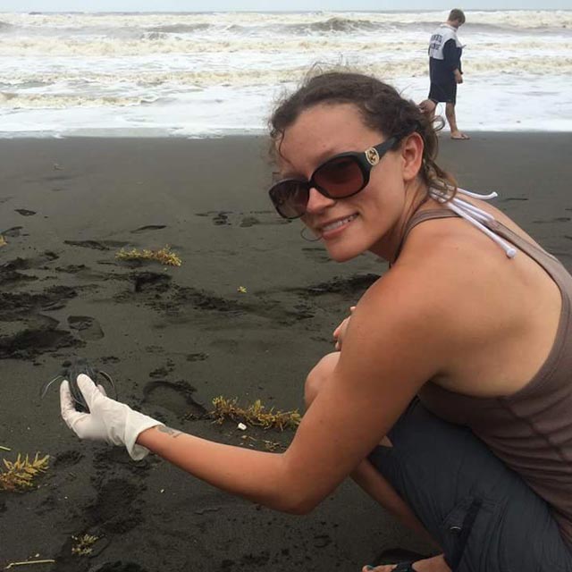 Keely Rodriguez on a beach holding a baby sea tortoise.