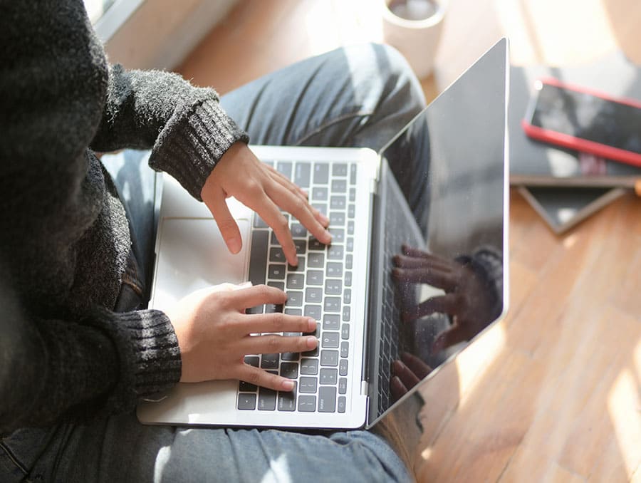 Student sitting on floor using laptop to access Zoom.