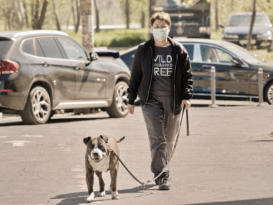 a woman wearing a mask while walking a dog