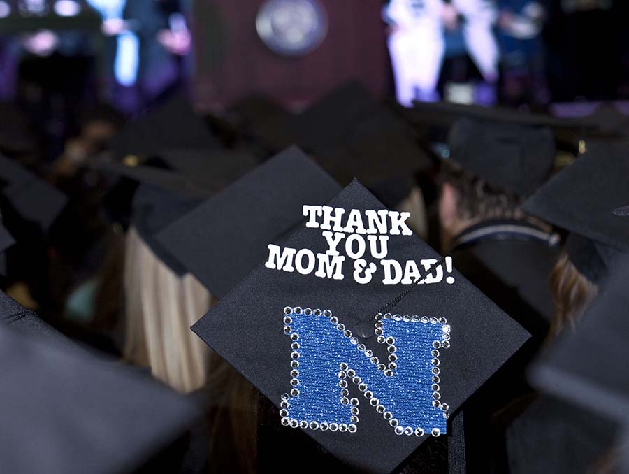 Thank you Mom & Dad! written on a black mortar board commencement cap at an indoor graduation ceremony.