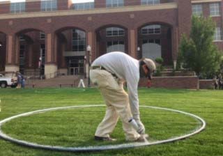 Person painting social distancing circles on a lawn.