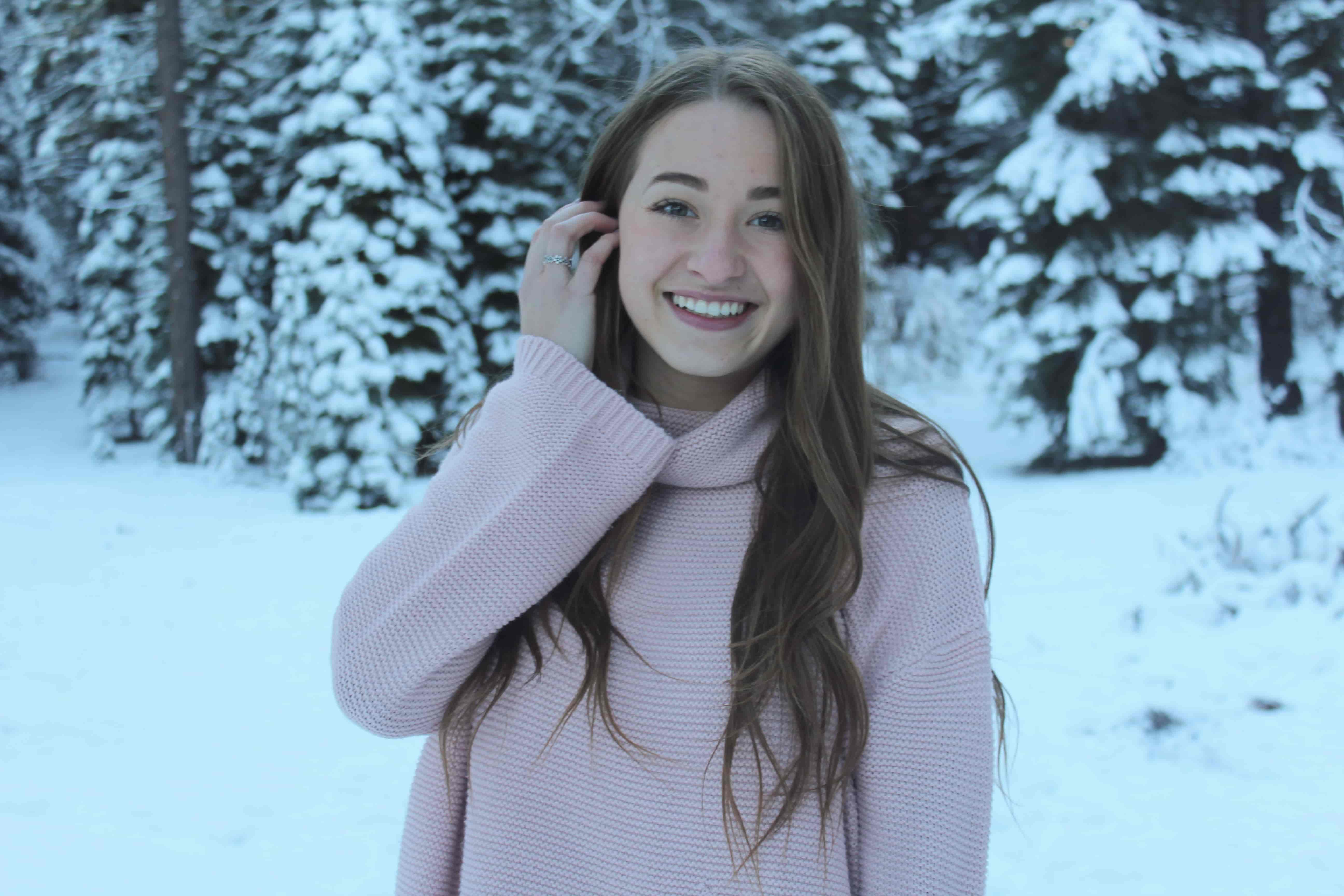 Portrait of a woman smiling at the camera, standing in front of snow covered pine trees