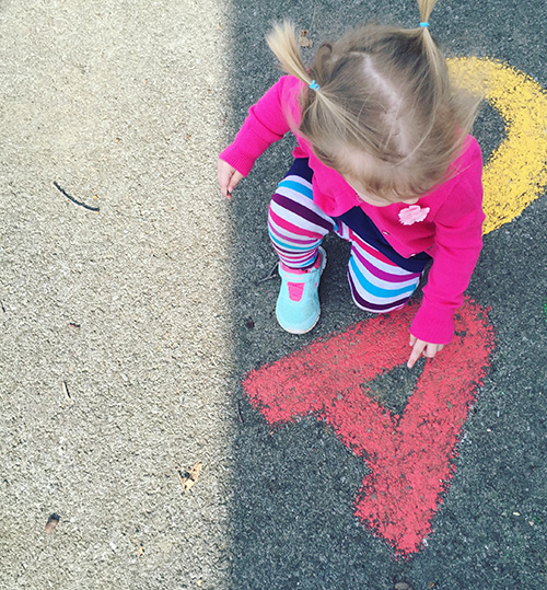 Child pointing to the letter "A" written in chalk on concrete