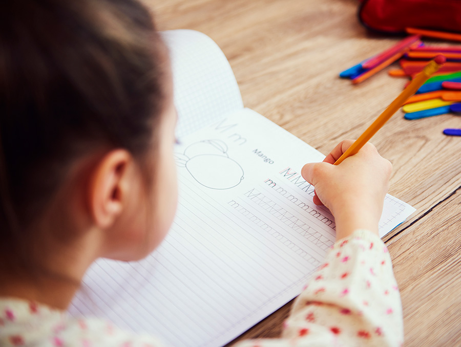 Student working on writing letters on a piece of paper at a desk