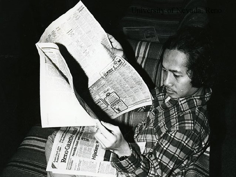 Unidentified University of Nevada, Reno student reading a newspaper while sitting on a couch