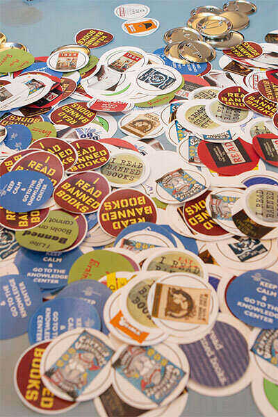 Colorful and circular shaped paper designs scattered across a table to be used to create wearable buttons as part of the Libraries Edible Books Festival which is part of Banned Books Week.