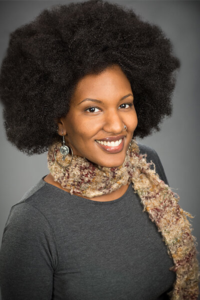 African-American woman wearing a grey sweater and beige neck scarf 