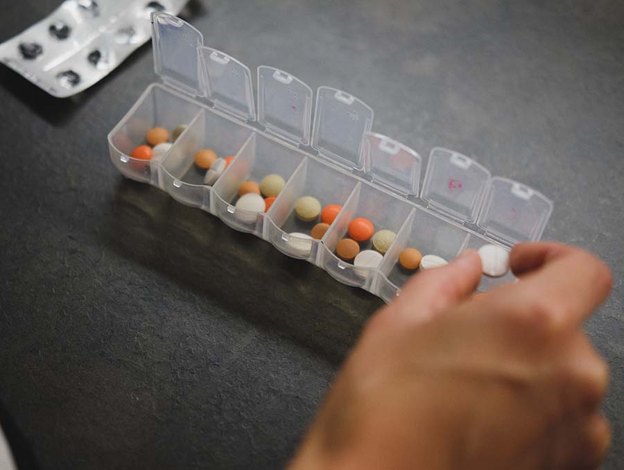 Person about to pick medicine from medicine organizer. Photo by Laurynas Mereckas.